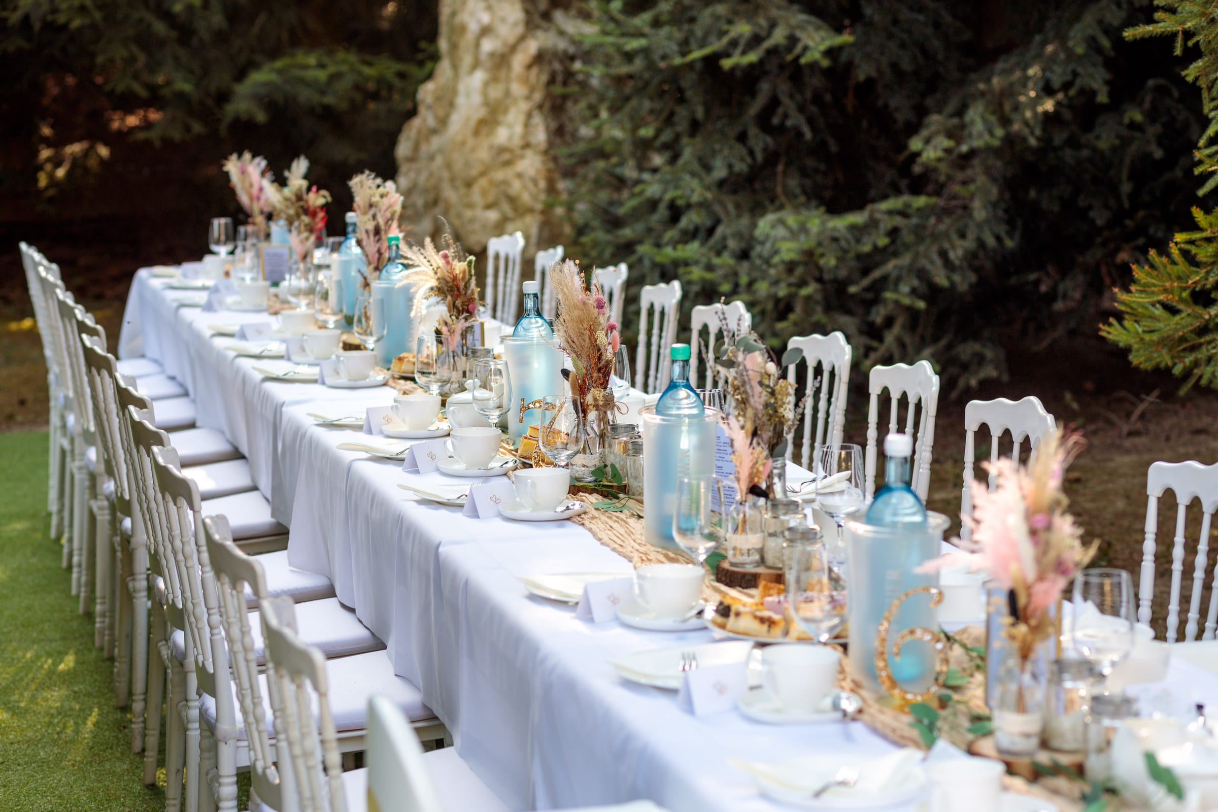 Lange, weiß eingedeckte Festtafel im Park mit Tannenwald