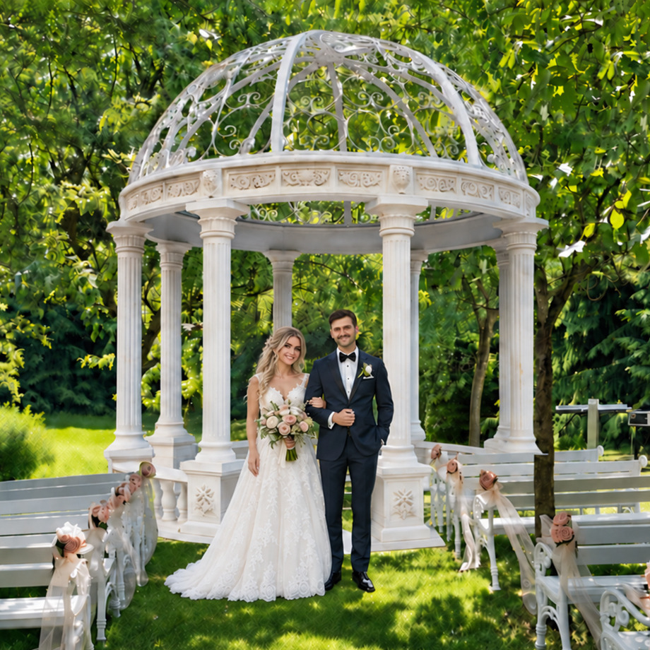 Brautpaar vor dem weißen Marmorpavillon im Wedding-Garden, davor weiße Bänke mit Rosenschmuck